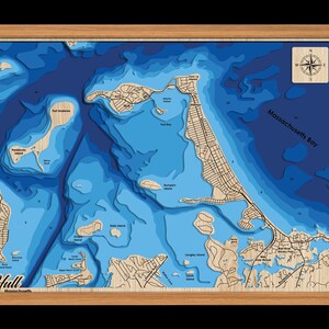 May include: A wooden 3D relief map of Hull, Massachusetts, showing the coastline and surrounding islands. The map is painted in shades of blue to represent the depth of the water. The map is framed in a light wood frame.