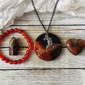 Peut inclure: Un bracelet en cornaline rouge, un pendentif en cornaline rouge, noir et brun avec un charme de croissant de lune argenté et un cœur en cornaline rouge, brun et vert.
