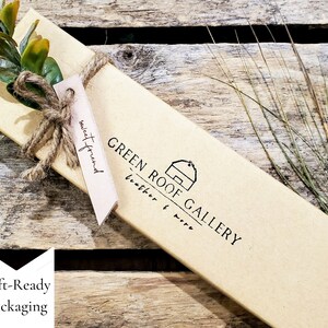 May include: A brown cardboard box with a gift tag that says "sweet friend". The box is tied with twine and has a green sprig of leaves on top. The box has a logo that says "GREEN ROOF GALLERY leather & wire".