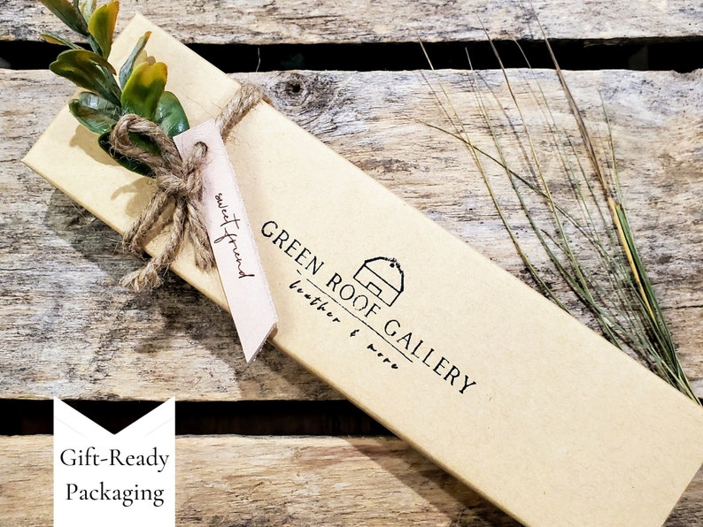 May include: A brown cardboard box with a gift tag that says "sweet friend". The box is tied with twine and has a green sprig of leaves on top. The box has a logo that says "GREEN ROOF GALLERY leather & wire".