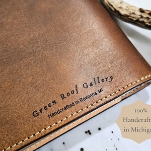 Puede incluir: Un diario de cuero marr&oacute;n con el texto "Green Roof Gallery Handcrafted in Ravenna, MI" grabado en la portada.