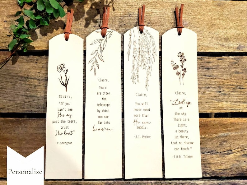 May include: Four wooden bookmarks with a white background and brown leather straps. Each bookmark features a different floral design and a quote. The quotes are: "If you can't see His way past the tears, trust His heart." - C. Spurgeon, "Tears are often the telescope by which men see far into heaven." - C. Spurgeon, "You will never need more than He can supply." - J.I. Packer, "Look up at the sky. There is a light, a beauty up there, that no shadow can touch." - J.R.R. Tolkien.