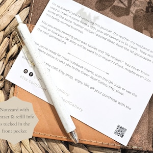 Puede incluir: Un diario blanco con una cubierta de cuero marr&oacute;n y una tarjeta metida en el bolsillo delantero. El diario tiene un c&oacute;digo QR y texto que dice "&iexcl;Estoy tan agradecida de que est&eacute;s recibiendo este diario! El cuero que mi esposo y yo usamos para hacerlo proviene de una curtidur&iacute;a de 100 a&ntilde;os en St. Louis. Todav&iacute;a usan algunas de las mismas "recetas de cuero" transmitidas de la primera generaci&oacute;n en este negocio familiar. Que disfrutes escribiendo tus propias historias y "recetas de vida". Nunca se sabe cu&aacute;ndo o c&oacute;mo se usar&aacute; tu historia de vida para impactar a otros... tal vez incluso en las pr&oacute;ximas generaciones. Cuando est&eacute;s listo para m&aacute;s insertos de cuaderno, escanea el c&oacute;digo QR o usa el sitio web a continuaci&oacute;n para ir a la tienda Etsy de Green Roof Gallery.  la tienda Etsy CRG, disfruta de un 10% de descuento en tu compra con el @gre etsy.com/shop..."