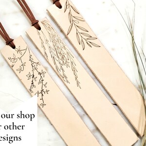 May include: Three leather bookmarks with brown tassels and delicate floral designs. The bookmarks are light brown and have a natural, rustic look.