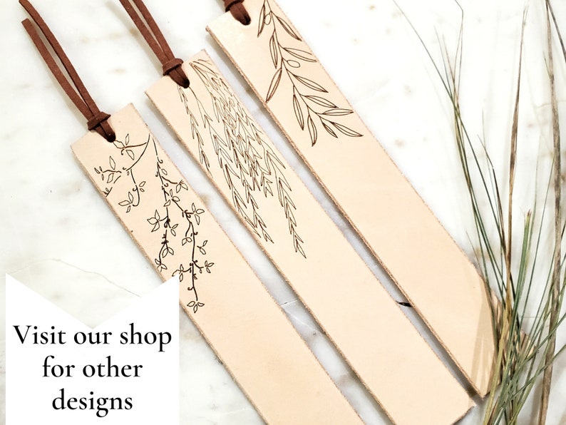 May include: Three leather bookmarks with brown tassels and delicate floral designs. The bookmarks are light brown and have a natural, rustic look.