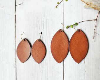 May include: Three pairs of leather earrings in a teardrop shape. The earrings are brown and have a gold-toned hook closure.