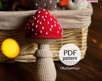 May include: A handmade crochet mushroom toy with a red cap and white spots. The mushroom has a beige stem and is displayed in front of a wicker basket. The image includes the text "PDF pattern" and the shop name "OlyaSamToys".