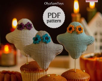 May include: Crocheted ghost cupcake toppers in grey, white, and blue, each with flower accents. The toppers sit atop cupcakes with gold sprinkles. The image includes the text "PDF pattern" and the seller's name.