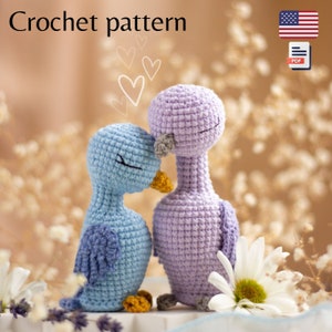 May include: Crochet pattern for two amigurumi birds, one light blue and one lavender, with closed eyes and beaks. The birds are cuddling together with hearts in the background. The pattern is available as a PDF download.