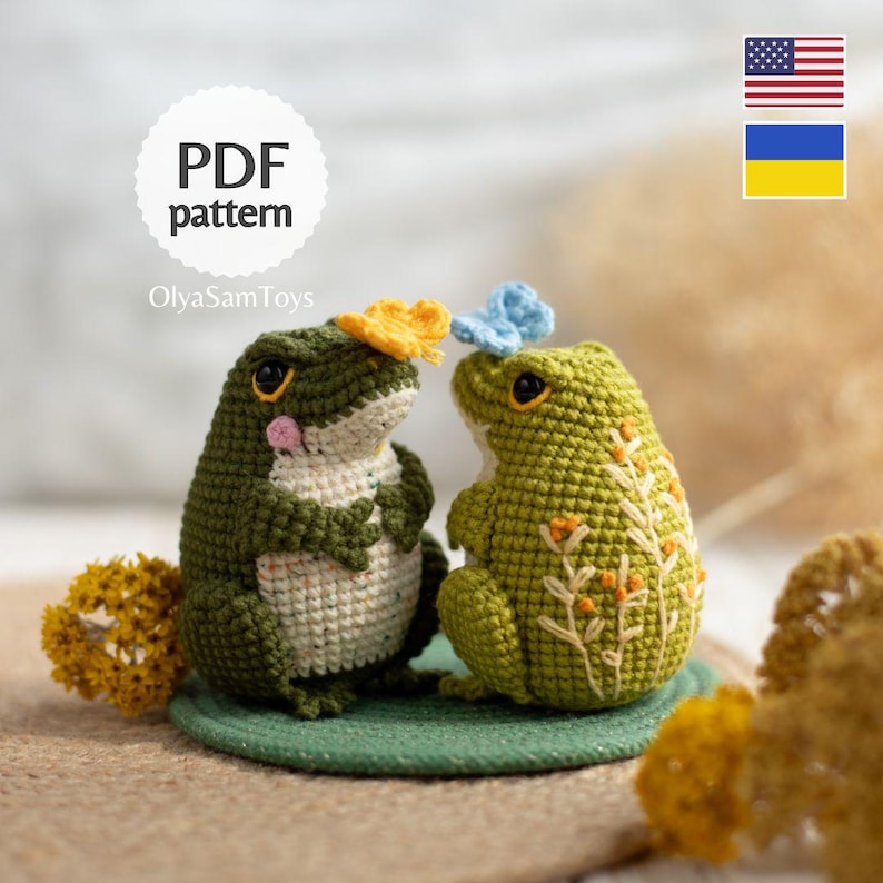 Puede incluir: Dos figuras de rana de ganchillo hechas a mano. Una rana es de color verde oscuro con una flor amarilla, la otra es de color verde claro con una flor azul. Las ranas est&aacute;n sobre una alfombra verde. Incluye el texto "PDF pattern" y "OlyaSamToys".