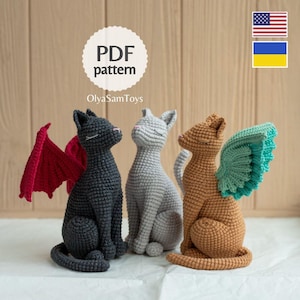 May include: Three crocheted cat figurines in black, light gray, and tan. The black cat has red wings, the tan cat has teal wings, and the gray cat is wingless. Each cat has closed eyes and a seated posture. Text reads PDF pattern OlyaSamToys.