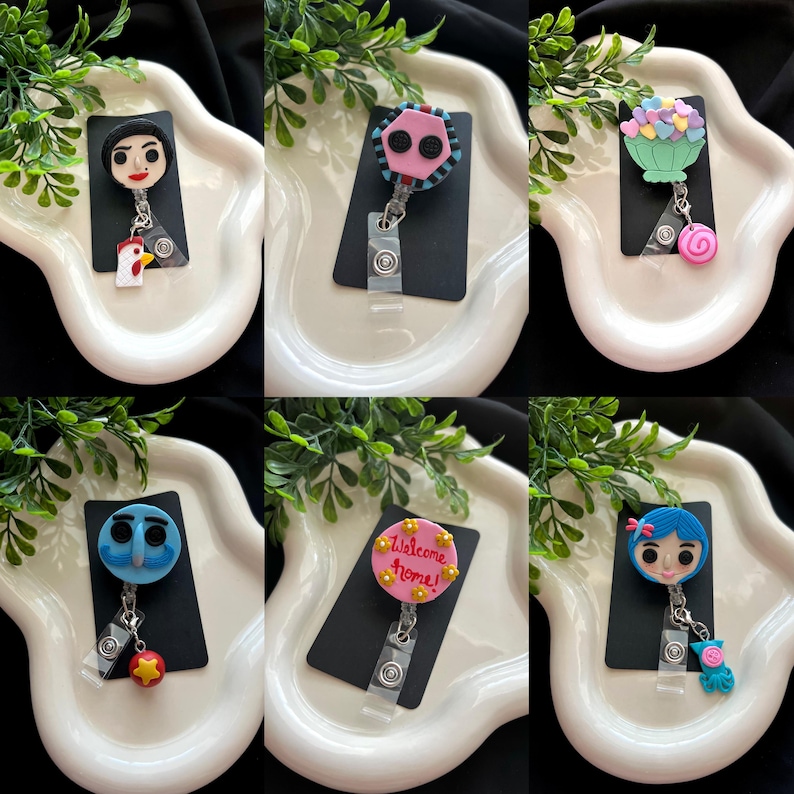 May include: A collection of six handmade badge reels with various character designs. Each reel features a unique character, including a girl, a rooster, and a character with the text "Welcome home!". The reels are attached to black rectangular cards.