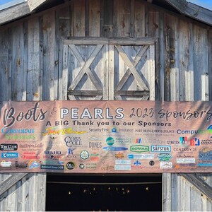 May include: A brown wooden barn with a banner that reads "Boots & PEARLS 2023 Sponsors" and lists a variety of sponsors. The banner is brown with white text and logos.