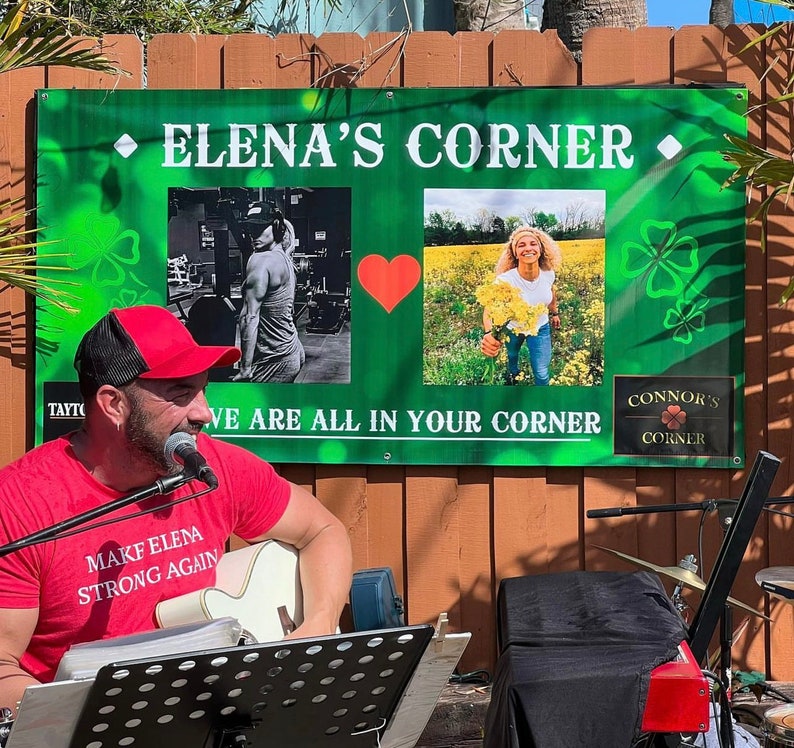 May include: A green sign with the text "Elena's Corner" and two smaller images. The left image shows a person lifting weights. The right image shows a woman standing in a field of flowers. The text "We are all in your corner" is below the images. A man is playing a guitar in front of the sign.