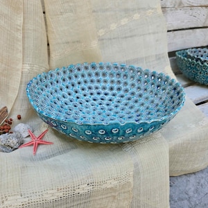 Op de afbeelding: Een ronde keramische kom met een levendig turquoise en blauw glazuur, voorzien van een herhalend reliëfpatroon van bloemen of sterren over het gehele binnen- en buitenoppervlak, met een geschulpte rand en een diepe, brede komvorm.