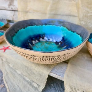 Może przedstawiać: Zestaw ceramicznych misek o morskim designie. Miski mają turkusowe i niebieskie wnętrze, ciemnoszarą obw&oacute;dkę i beżowy zewnętrzny wz&oacute;r. Widoczna jest czerwona rozgwiazda.