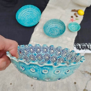 May include: A set of three blue ceramic bowls with a decorative floral pattern. The bowls are all different sizes and have a scalloped edge.