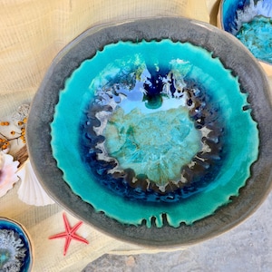 Może przedstawiać: Ceramiczna miska o unikalnym designie. Miska ma żywe turkusowe wnętrze, ciemnoniebieski i brązowy środek oraz szarą obw&oacute;dkę. Muszle, czerwona rozgwiazda i inne elementy dekoracyjne otaczają miskę.
