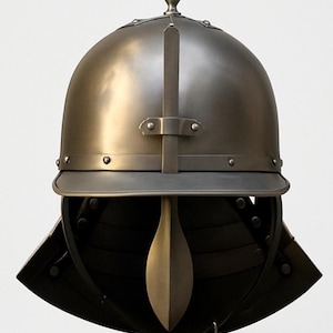 Op de afbeelding: Een metaalgrijze helm met een afgeronde bovenkant, een vizier en een decoratieve bekroning. De helm heeft een geklonken band rond de basis en een verticale band over de bovenkant. Het onderste deel van de helm is zwart.
