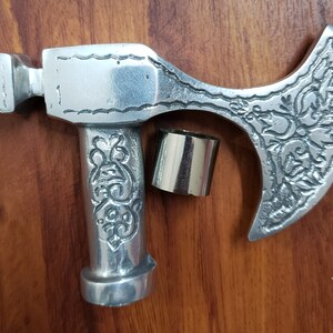 Puede incluir: Cabeza de hacha de plata con un dise&ntilde;o ornamentado. La cabeza del hacha est&aacute; unida a un mango de plata con un dise&ntilde;o decorativo. La cabeza del hacha mide aproximadamente 25 cm de largo y el mango aproximadamente 15 cm.
