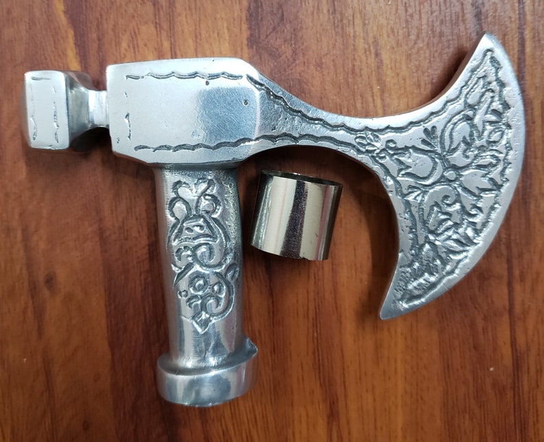 Puede incluir: Cabeza de hacha de plata con un dise&ntilde;o ornamentado. La cabeza del hacha est&aacute; unida a un mango de plata con un dise&ntilde;o decorativo. La cabeza del hacha mide aproximadamente 25 cm de largo y el mango aproximadamente 15 cm.