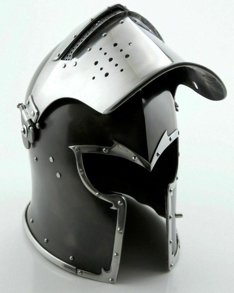 K&ouml;nnte beinhalten: Ein schwarz-silberner Helm mit Visier und einem klappbaren, spitzen Oberteil. Der Helm hat ein dekoratives Design mit Nieten und einer strukturierten Oberfl&auml;che.
