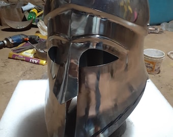 May include: A silver Spartan helmet with a pointed crest and a face mask with eye holes. The helmet is made of metal and has a shiny finish.