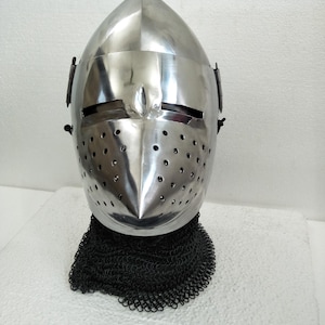 May include: A silver helmet with a pointed top and a face mask with holes. The helmet is on a stand with a black chainmail neck guard.