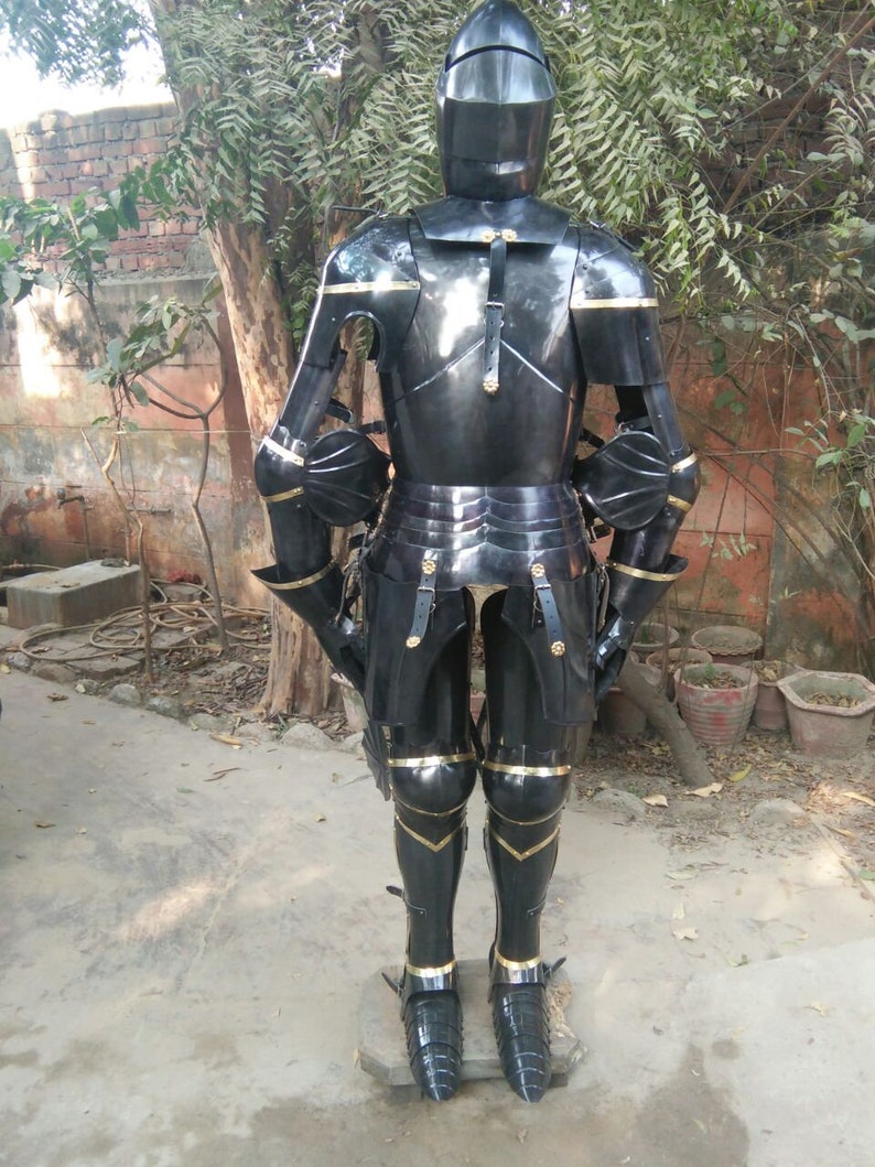May include: Full body suit of black armour with gold accents. The armour includes a helmet, breastplate, gauntlets, and greaves. The armour is standing on a concrete surface.