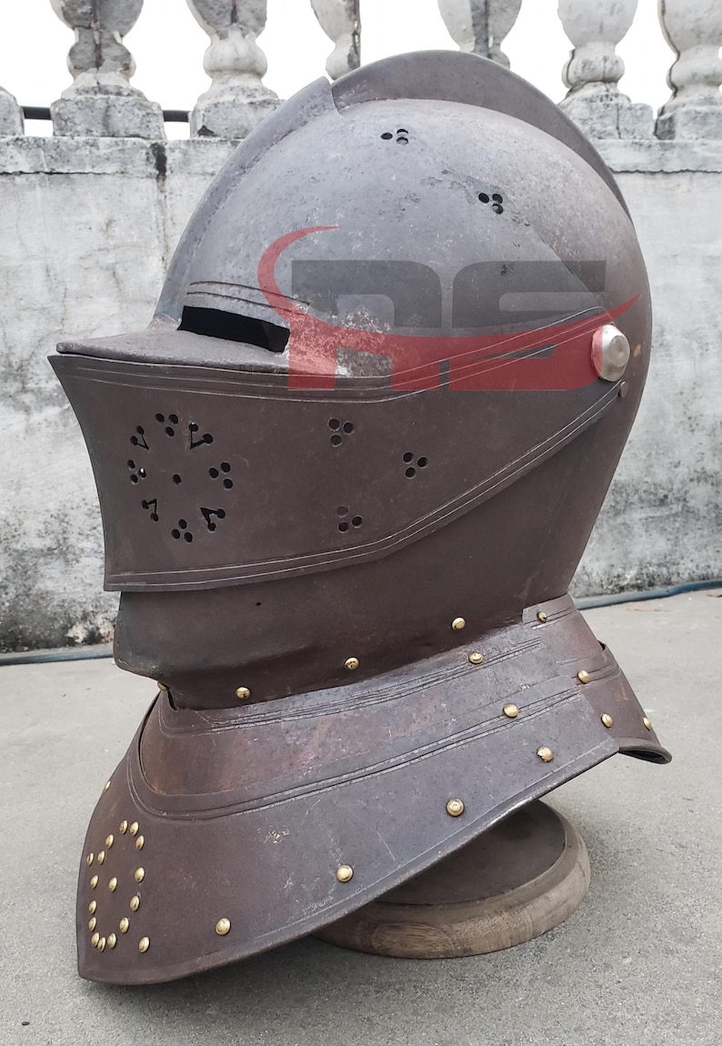 Puede incluir: Un casco de metal marr&oacute;n con visera y un dise&ntilde;o decorativo. El casco tiene un acabado en lat&oacute;n y est&aacute; sobre un soporte de madera.