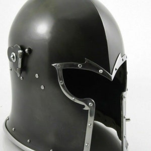 K&ouml;nnte beinhalten: Ein schwarzer Stahlhelm mit Visier und einer klappbaren Gesichtsplatte. Der Helm hat eine strukturierte Oberfl&auml;che und ist mit Nieten verziert.
