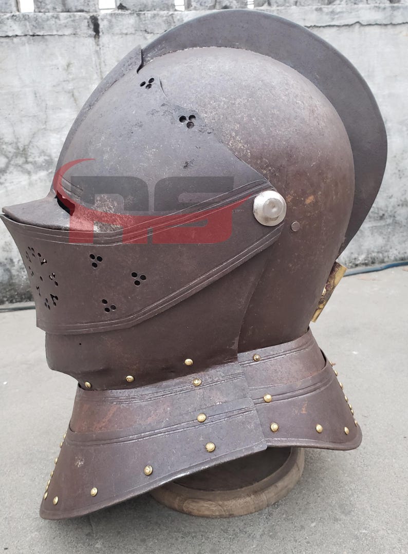 Puede incluir: Un casco de metal marr&oacute;n con visera y parte superior puntiaguda. El casco tiene un borde de lat&oacute;n y est&aacute; decorado con remaches. El casco est&aacute; sobre un soporte de madera.