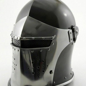 K&ouml;nnte beinhalten: Ein schwarz-silberner Helm mit Visier und einem Maschengesichtsgitter. Der Helm hat ein klappbares Visier und ein dekoratives Design auf der Oberseite.