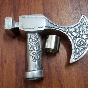 Puede incluir: Un bast&oacute;n de paseo de metal plateado en forma de hacha con un dise&ntilde;o ornamentado y una tapa de metal plateado en el mango.