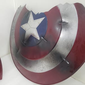 May include: A red, white, and blue Captain America shield with a star in the center. The shield is damaged and has a chipped edge.