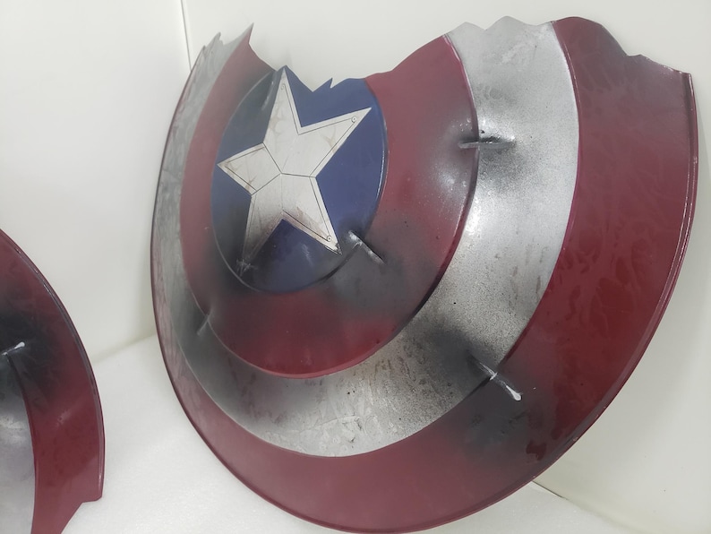 May include: A red, white, and blue Captain America shield with a star in the center. The shield is damaged and has a chipped edge.