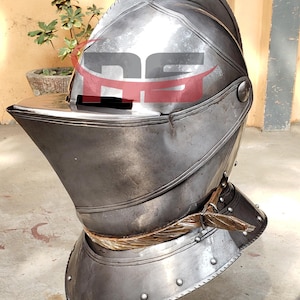 May include: A silver helmet with a visor and a brown leather strap. The helmet is on a black stand.