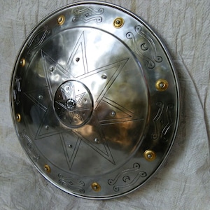 May include: A silver round shield with a large eight-pointed star design in the center. The shield has a decorative border with a repeating pattern of small circles and curved lines.