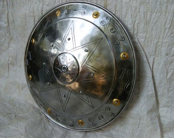 May include: A silver round shield with a large eight-pointed star design in the center. The shield has a decorative border with a repeating pattern of small circles and curved lines.