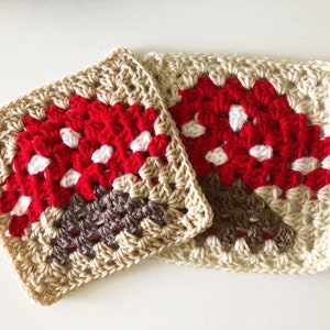 May include: Two crocheted squares in beige, brown, red, and white, resembling mushrooms. The squares are made with a granny stitch pattern.