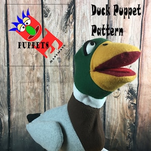 Puede incluir: Un títere de pato verde, amarillo y marrón con la boca abierta. El títere está de pie sobre una superficie de madera. El texto "Duck Puppet Pattern" está escrito en letras negras sobre el títere. El texto "Patterns for foam and fabric" está escrito en letras negras debajo del títere.