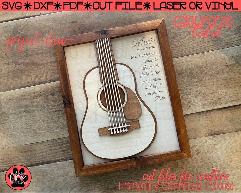 May include: A wooden frame with a white background and a cutout of an acoustic guitar. The quote "Music gives a soul to the universe. Wings to the mind, flight to the imagination and life to everything. -Plato" is printed on the background. The frame is on a wooden surface.