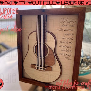 May include: A wooden framed picture with a laser cut design of an acoustic guitar and a quote about music by Plato. The quote reads "Music gives a soul to the universe, wings to the mind, flight to the imagination and life to everything. -Plato".