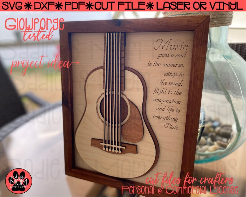 May include: A wooden framed picture with a laser cut design of an acoustic guitar and a quote about music by Plato. The quote reads "Music gives a soul to the universe, wings to the mind, flight to the imagination and life to everything. -Plato".