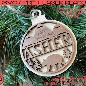 Peut inclure: Une décoration de Noël en bois avec un ours brun, des montagnes et le texte "2021 Premier Noël Asher".