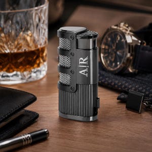 May include: A gunmetal gray metal lighter featuring a vertical ribbed texture on the lower body and a silver mesh panel on the upper side. The lighter is engraved with the letters AJR in a serif font on the smooth central section of the casing.