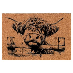 May include: A black and white illustration of a Highland cow peeking over a wooden fence. The cow has a fluffy mane and a friendly expression.