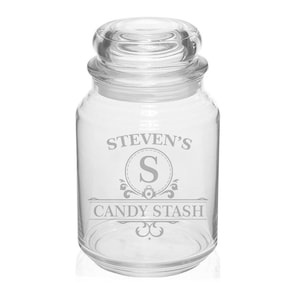 May include: A clear glass candy jar with a lid. The jar has the text "STEVEN'S" above a decorative emblem with the letter "S" inside, and the words "CANDY STASH" below. The jar is designed to store candy.