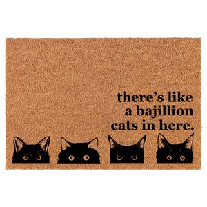 May include: A brown coir doormat with the text "there's like a bajillion cats in here." Four black cat silhouettes peek out from behind the bottom edge of the mat.