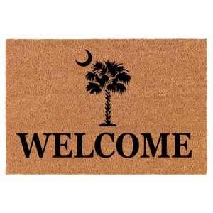May include: A brown coir doormat with the text "WELCOME" in black lettering. A black silhouette of a palm tree with a crescent moon above it is centered above the text.
